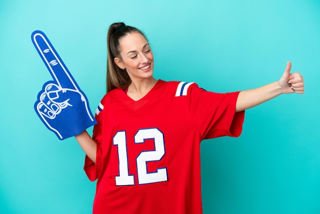 Young caucasian sport woman isolated on blue background giving a thumbs up gesture