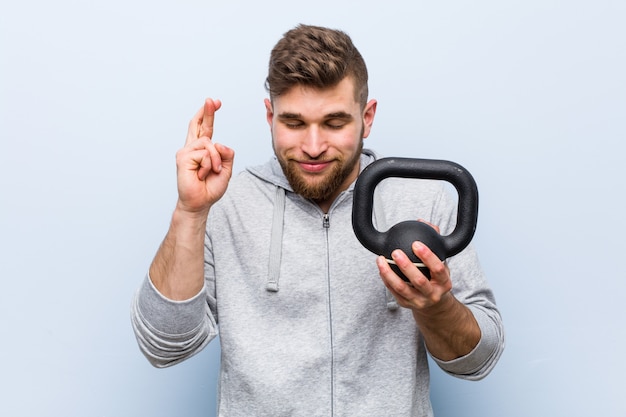 Young caucasian sportsman holding a dumbbell crossing fingers for having luck