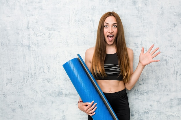 Young caucasian sportswoman holding a mat celebrating a victory or success