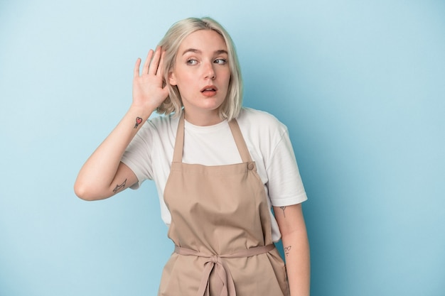 Young caucasian store clerk woman isolated on blue background trying to listening a gossip.