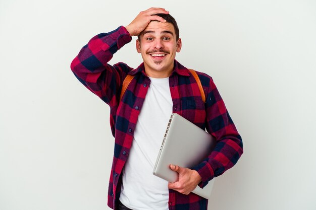 L'uomo giovane studente caucasico che tiene un computer portatile isolato su priorità bassa bianca ride con gioia mantenendo le mani sulla testa. concetto di felicità.