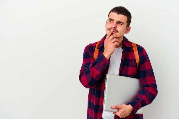 Young caucasian student man holding a laptop isolated on white wall making up plan in mind, setting up an idea.