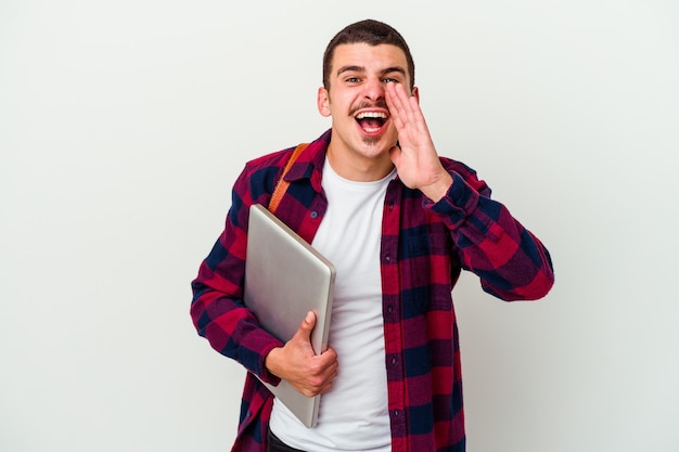 Uomo giovane studente caucasico che tiene un computer portatile isolato sul muro bianco che grida eccitato di fronte.