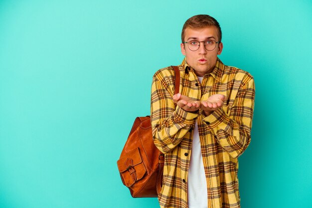 Uomo giovane studente caucasico isolato su labbra pieghevoli blu e tenendo i palmi per inviare un bacio d'aria.