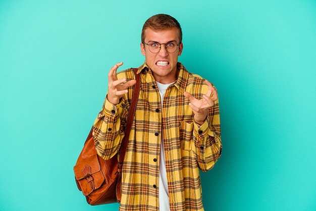 Young caucasian student man isolated on blue wall upset screaming with tense hands.