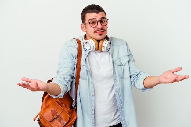 Giovane studente caucasico che ascolta musica isolato su bianco dubitando e alzando le spalle nel gesto interrogativo.