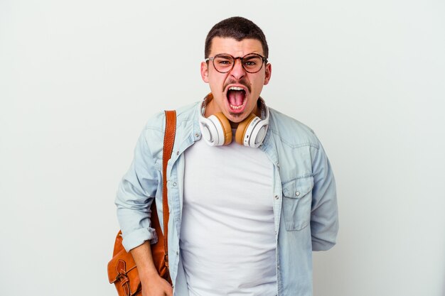 Young caucasian student man listening to music on white screaming very angry and aggressive.