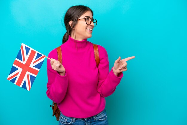 青の背景に英語の旗を保持している若い白人学生の女性は、指を横に向けて製品を提示します