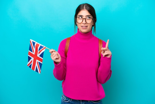 파란색 배경에 격리된 영어 깃발을 들고 손가락을 가리키는 아이디어를 생각하는 젊은 백인 학생 여성