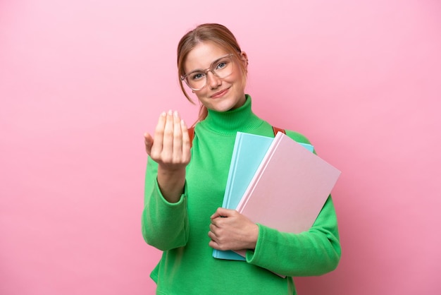 Young caucasian student woman isolated on pink background inviting to come with hand Happy that you came