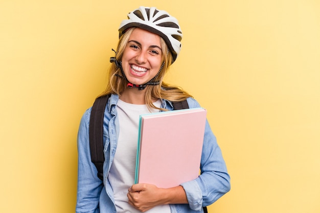 黄色の背景に分離された自転車のヘルメットを身に着けている若い白人学生女性は幸せ、笑顔、陽気な。