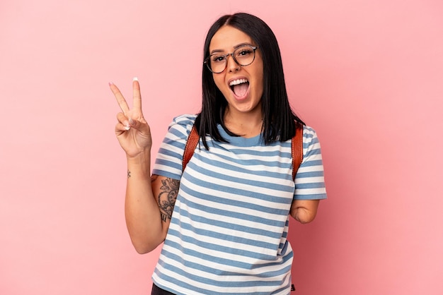 Young caucasian student woman with one arm isolated on pink background joyful and carefree showing a peace symbol with fingers.