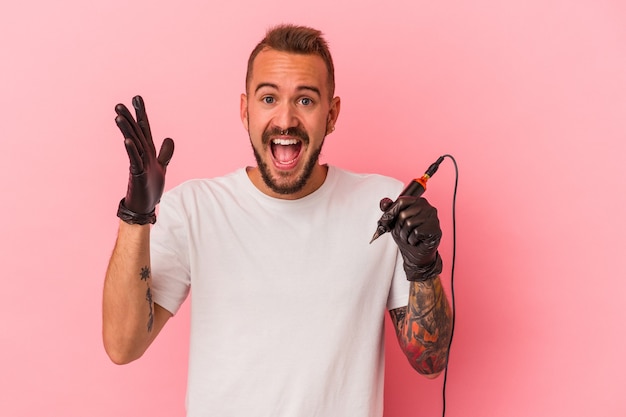 Young caucasian tattoo artist isolated on pink background  receiving a pleasant surprise, excited and raising hands.