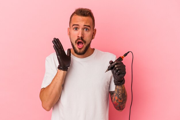 Young caucasian tattoo artist isolated on pink background  surprised and shocked.