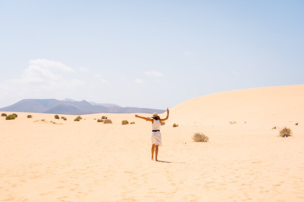 A young Caucasian tourist in a white dress and a hat walking through the dunes of the Corralejo Natural Park, Fuerteventura, Canary Islands. Spain