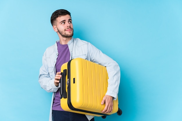 Young caucasian traveler man holding a suitcase isolated dreaming of achieving goals and purposes