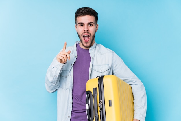 Young caucasian traveler man holding a suitcase isolated having an idea, inspiration concept.