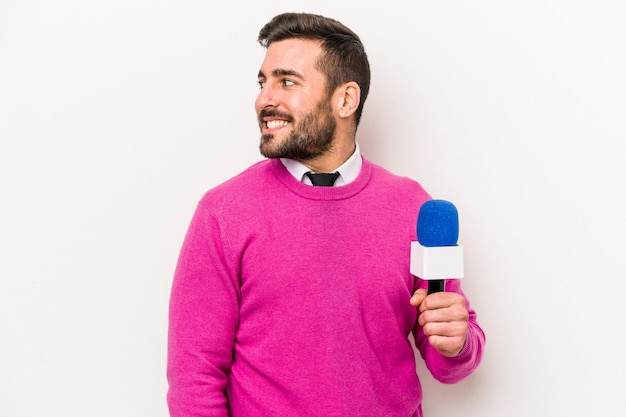 Young caucasian tv presenter man isolated on white background looks aside smiling cheerful and pleasant