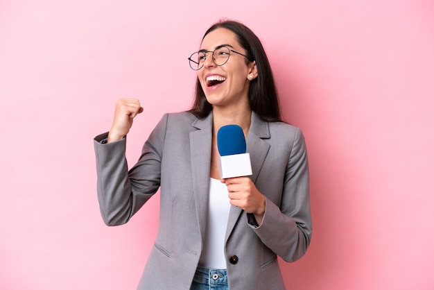 Young caucasian tv presenter woman isolated on pink background\
celebrating a victory in winner position