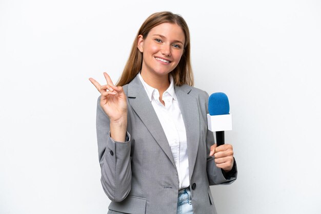 Young caucasian tv presenter woman isolated on white background\
smiling and showing victory sign