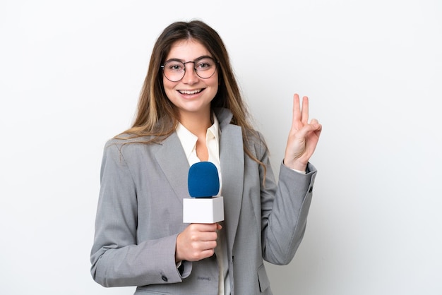 Foto giovane donna caucasica presentatore televisivo isolata su sfondo bianco sorridente e mostrando il segno della vittoria