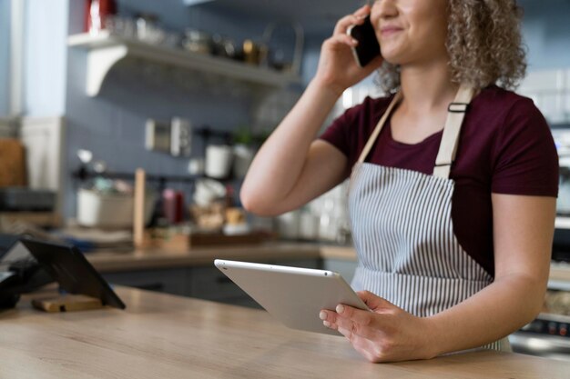 Foto giovane cameriera caucasica che usa tablet digitale e telefono al lavoro nel caffè