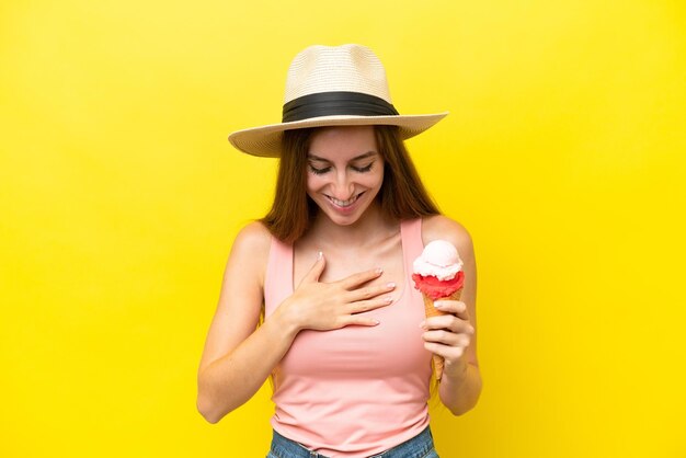 Young caucasian with a cornet ice cream isolated on yellow background smiling a lot