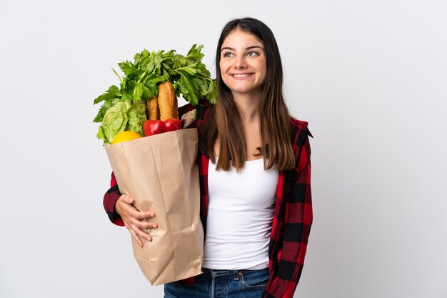 Young caucasian with vegetables isolated on white wall thinking an idea while looking up