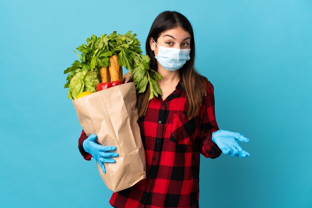 青で隔離の野菜とマスクを持つ若い白人は、肩を持ち上げながら疑いのジェスチャーをします