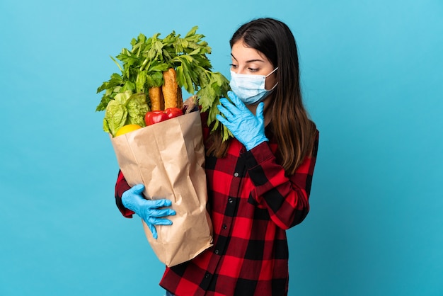 Young caucasian with vegetables and mask isolated on blue with surprise and shocked facial expression