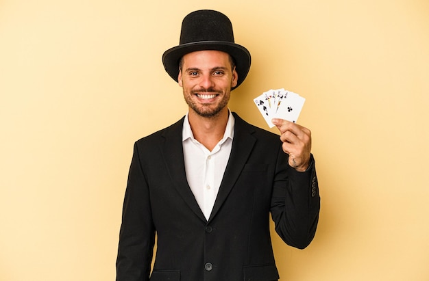 Young caucasian wizard holding magic card isolated on yellow\
background happy, smiling and cheerful.