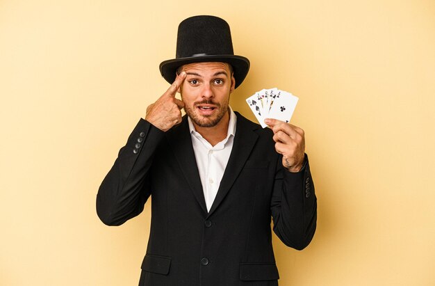 Young caucasian wizard holding magic card isolated on yellow background showing a disappointment gesture with forefinger.