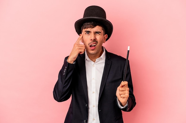 Young caucasian wizard man holding a wand isolated on pink background showing a disappointment gesture with forefinger.