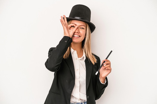 Young caucasian wizard woman holding wand isolated on white background excited keeping ok gesture on eye.