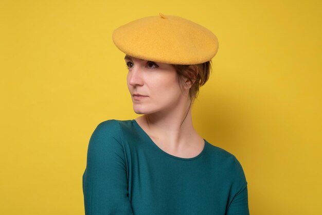 Young caucasian woamn wearing yellow beret with serious expression on face Simple and natural looking Studio shot on yellow wall