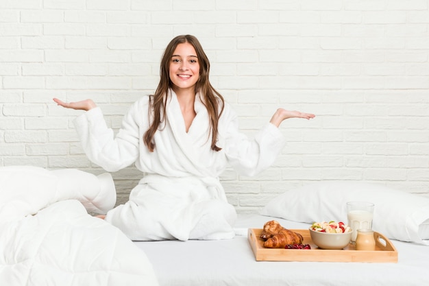 Young caucasian woman on the bed makes scale with arms, feels happy and confident.