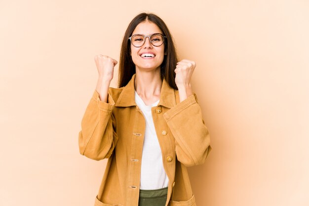 Young caucasian woman on beige wall cheering carefree and excited