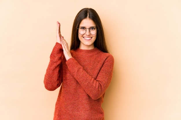 Young caucasian woman on beige wall feeling energetic and comfortable, rubbing hands confident