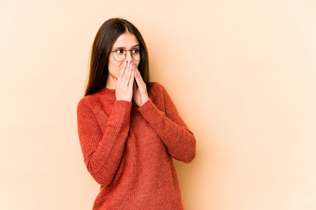 Young caucasian woman on beige wall laughing about something, covering mouth with hands.