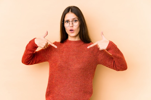 La giovane donna caucasica sulla parete beige indica giù con le dita, la sensibilità positiva.