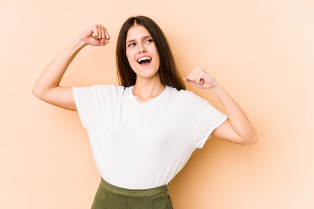 Young caucasian woman on beige wall raising fist after a victory