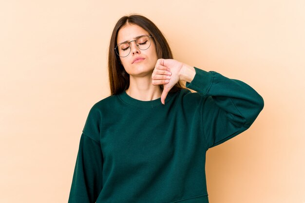 Young caucasian woman on beige wall showing a dislike gesture, thumbs down