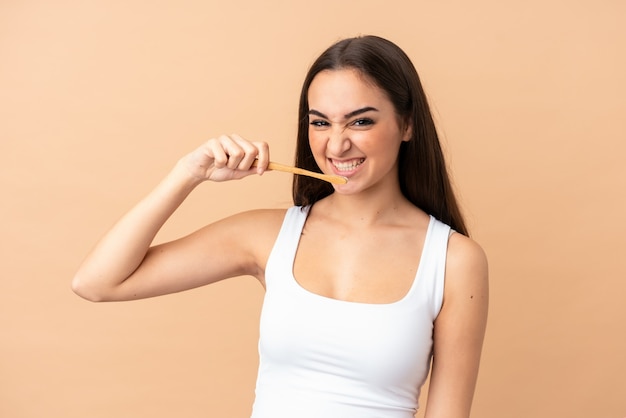 Young caucasian woman on beige wall with a toothbrush