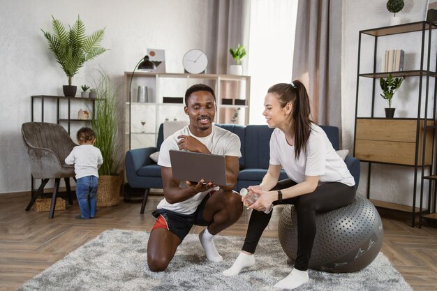 Young caucasian woman in black sports leggings and tshirt sitting on fit ball drinking water