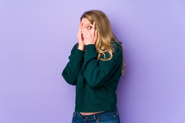 Young caucasian woman blink through fingers frightened and nervous.