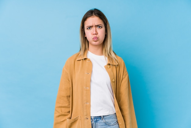 Young caucasian woman blows cheeks, has tired expression