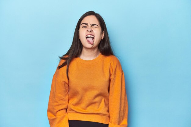 Young caucasian woman on blue backdrop funny and friendly sticking out tongue