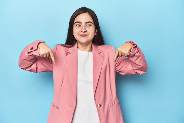 Young Caucasian woman on blue backdrop points down with fingers positive feeling