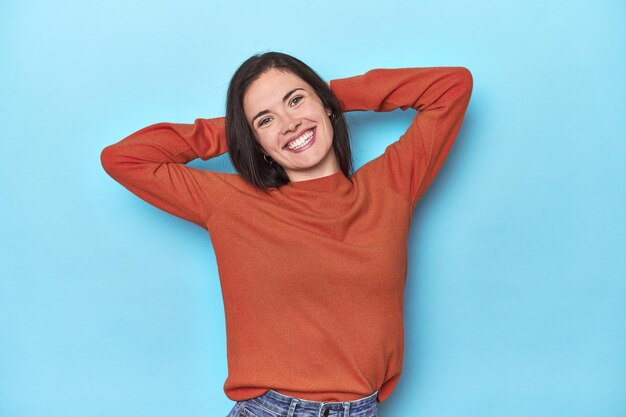 Young caucasian woman on blue backdrop stretching arms relaxed position