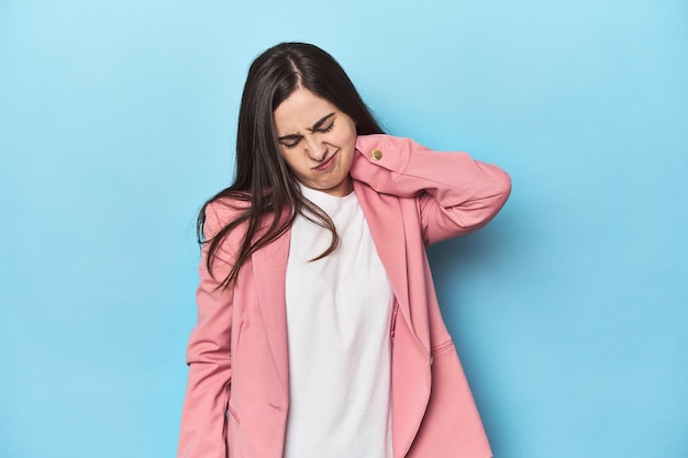 young caucasian woman on blue backdrop suffering neck pain due to sedentary lifestyle
